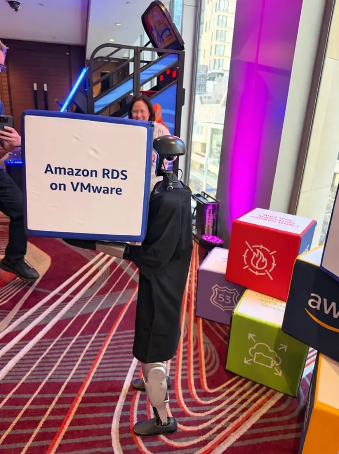 Rocco the humanoid, in a black robe, holding an Amazon RDS on VMware sign at the AWS event